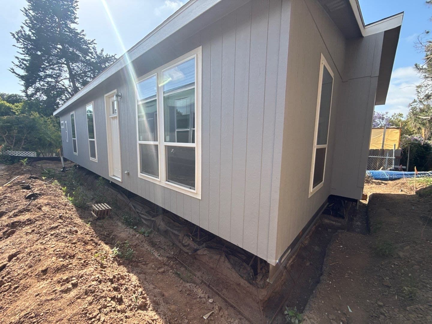 A newly installed manufactured home with grey siding and large windows.